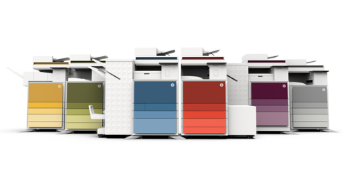 MODOX PRINT FOX Office Zwei moderne Multifunktionsdrucker stehen in einem gut beleuchteten Ausstellungsraum mit bunten Architekturfotos an den Wänden und Designelementen wie Akustikplatten und Computerarbeitsplätzen im Hintergrund.